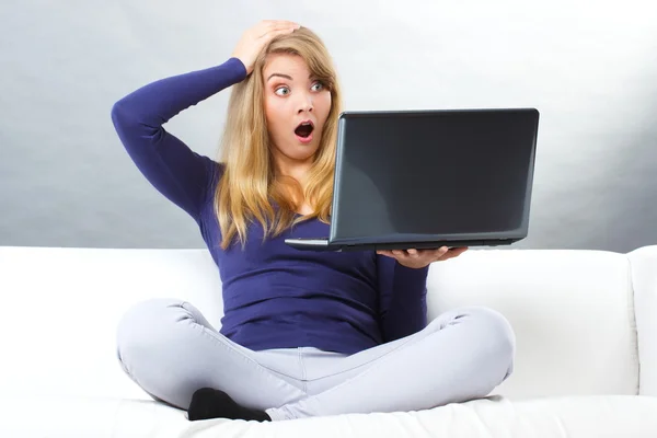 Mujer asustada sentada en el sofá y mirando a la computadora portátil, la tecnología moderna — Foto de Stock