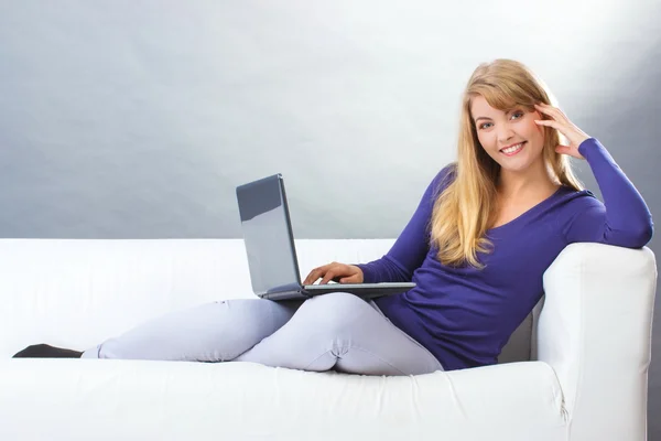 Donna felice utilizzando il computer portatile seduto sul divano, tecnologia moderna — Foto Stock