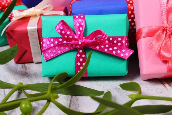 Wrapped colorful gifts for Christmas and mistletoe on old wooden background — Stock Photo, Image