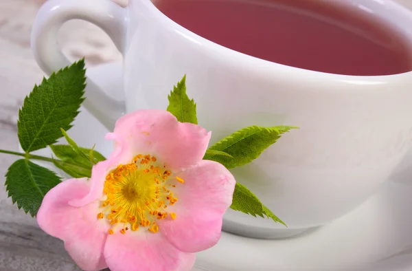 Tasse Tee mit wilder Rosenblüte auf altem rustikalem Holzhintergrund — Stockfoto