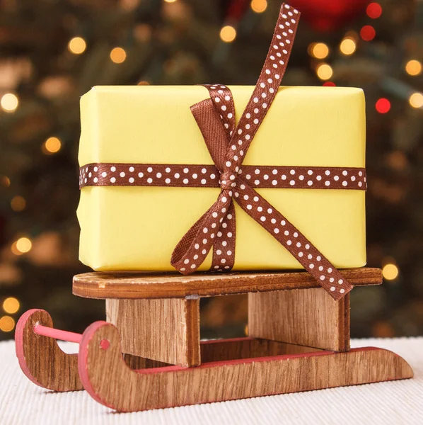 Radbruten gåva på trä släde och julgran med ljus i bakgrunden — Stockfoto