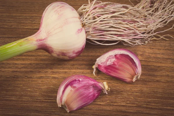 Vintage-Foto, ganzer Knoblauch mit Wurzeln und Nelken auf Holztisch — Stockfoto