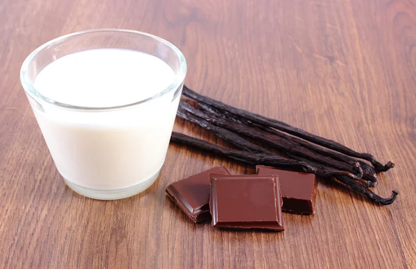 Dark chocolate, fragrant vanilla sticks and glass of milk on wooden surface plank — Stockfoto