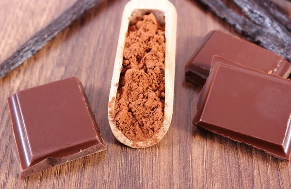 Powdery cocoa, dark chocolate, fragrant vanilla sticks on wooden surface — Stockfoto