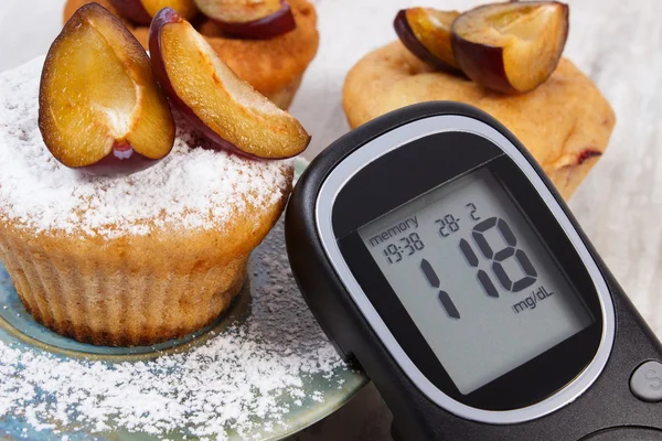 Glucometer, magdalenas con ciruelas y azúcar en polvo sobre fondo de madera, diabetes y delicioso postre — Foto de Stock