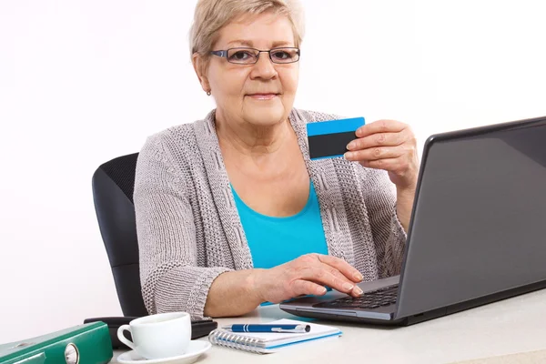 Elderly senior woman with credit card and laptop paying over internet for utility bills or online shopping