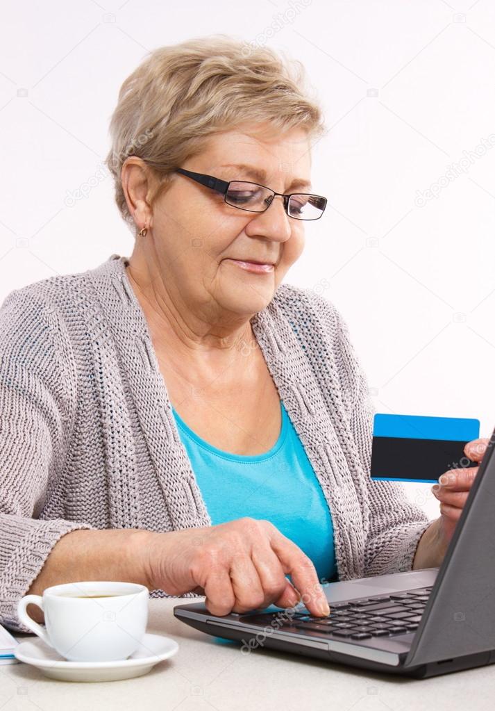 Elderly senior woman with credit card and laptop paying over internet for utility bills or online shopping