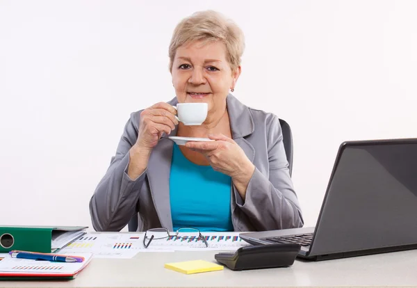 Ouderen zakenvrouw thee of koffie drinken bij balie in kantoor, pauze op het werk — Stockfoto