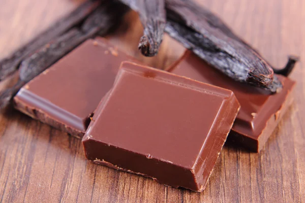 Chocolate escuro e palitos de baunilha perfumados na prancha de superfície de madeira — Fotografia de Stock