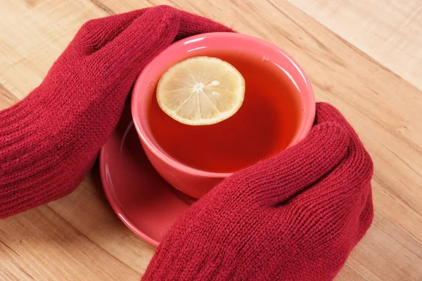 Mano de mujer en guantes de lana sosteniendo taza de té caliente en la mesa — Foto de Stock