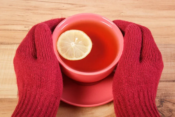 Mano de mujer en guantes de lana sosteniendo taza de té caliente en la mesa — Foto de Stock