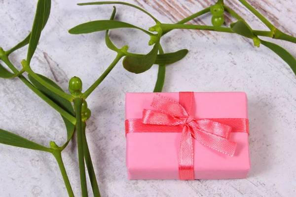 Wrapped pink gift for Christmas and mistletoe on old wooden background — Stock Photo, Image