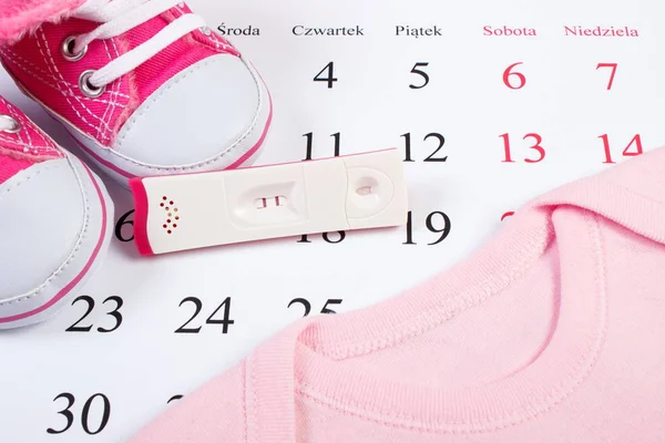 Pregnancy test with positive result and clothing for newborn on calendar, expecting for baby