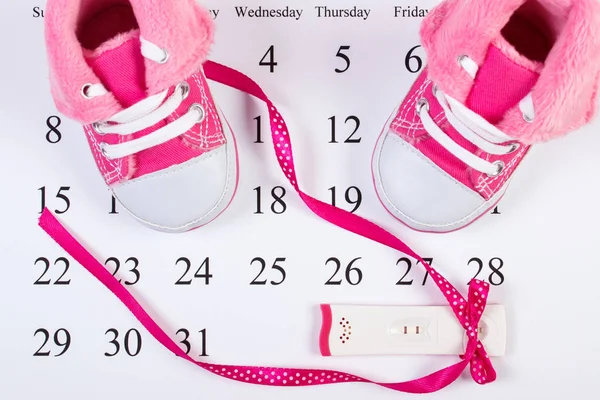 Tes kehamilan dengan hasil positif dan sepatu bayi pada kalender, mengharapkan bayi — Stok Foto