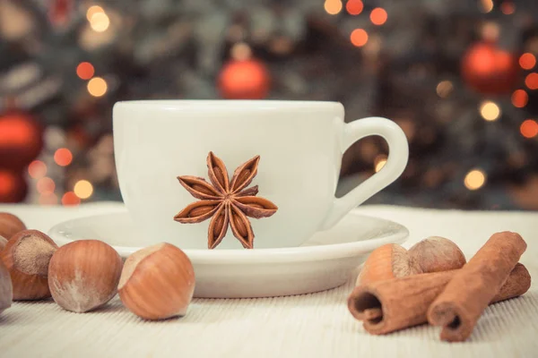 Hazelnuts, spices, cup of coffee or tea and christmas tree with lights in background