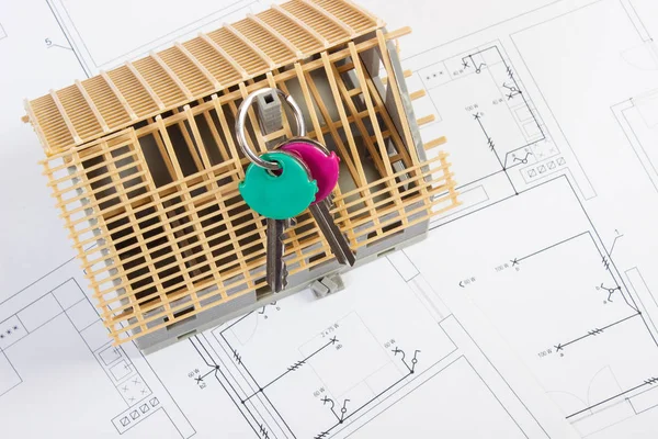 Ключи от дома и строящийся домик по электрическим чертежам, концепция строительства дома — стоковое фото