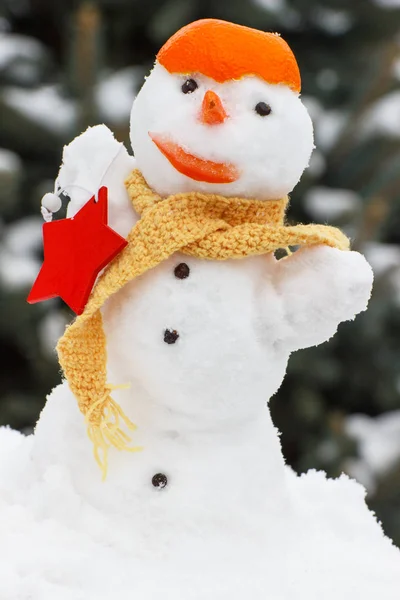 Inredda snögubbe med halsduk och tangerine peel, bakgrund av barrträd omfattas snö — Stockfoto