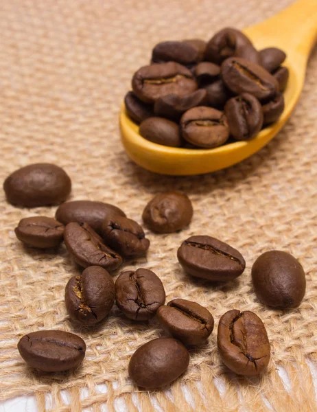Haufen Kaffeebohnen mit Holzlöffel auf Jutescreme — Stockfoto