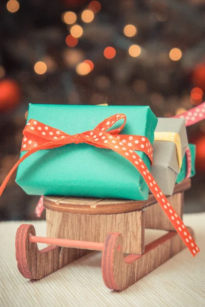 Foto vintage, presentes embrulhados coloridos em trenó de madeira e árvore de Natal com luzes no fundo — Fotografia de Stock
