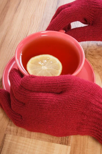 Mão de mulher em luvas de lã segurando xícara de chá quente na mesa — Fotografia de Stock