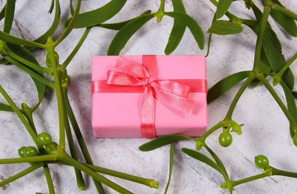 Wrapped pink gift for Christmas and mistletoe on old wooden background — Stock Photo, Image