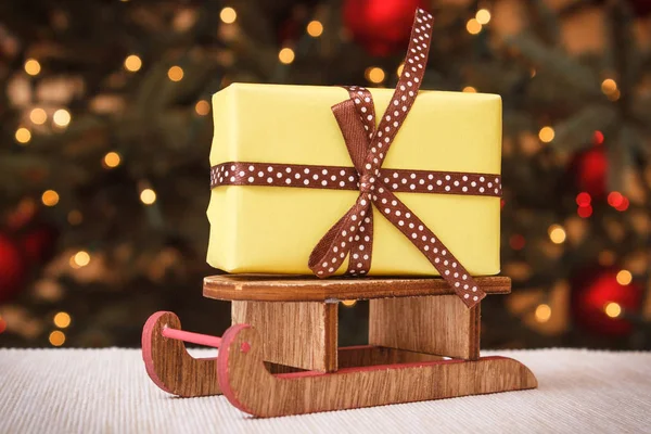 Radbruten gåva på trä släde och julgran med ljus i bakgrunden — Stockfoto