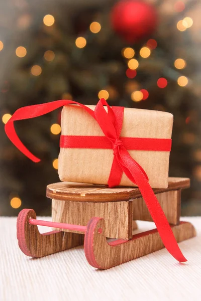 Regalo avvolto su slitta di legno e albero di Natale con luci sullo sfondo — Foto Stock