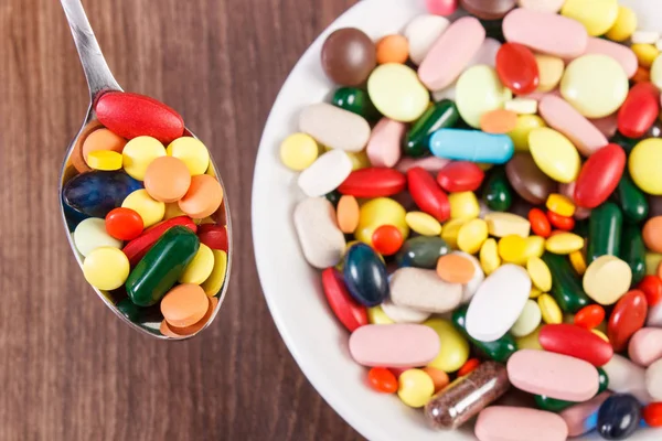 Píldoras médicas en cucharadita y montón de coloridas cápsulas médicas en segundo plano, concepto de atención médica —  Fotos de Stock