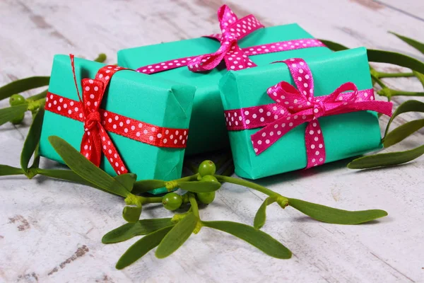 Wrapped green gifts for Christmas and mistletoe on old wooden background — Stock Photo, Image