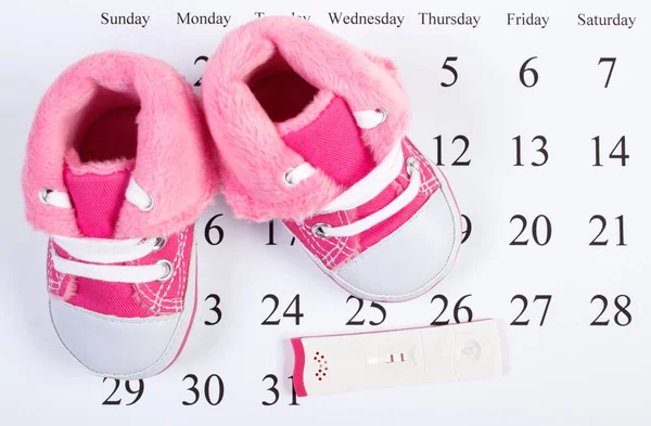 Teste de gravidez com resultado positivo e sapatos de bebê no calendário, esperando para o bebê — Fotografia de Stock