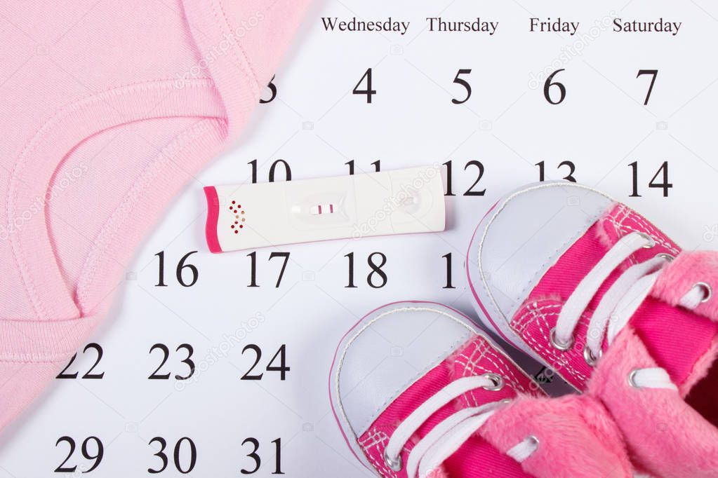 Pregnancy test with positive result and clothing for newborn on calendar, expecting for baby