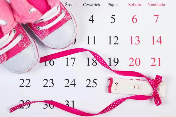 Test di gravidanza con esito positivo e scarpe per bambini sul calendario, in attesa per il bambino — Foto Stock