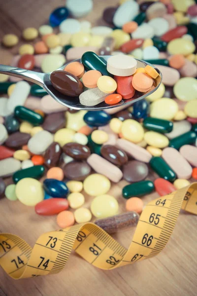 Pillole mediche su cucchiaino e mucchio di capsule mediche con centimetro, assistenza sanitaria e concetto di dimagrimento — Foto Stock