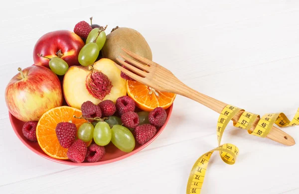 Свежие спелые фрукты на тарелке и вилке с сантиметром на досках — стоковое фото