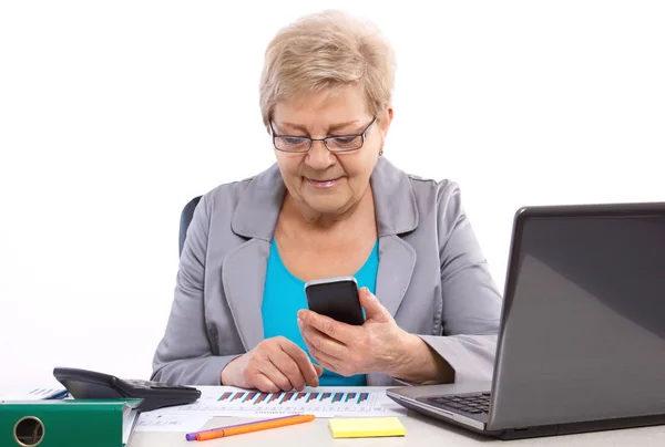 Cep telefonu kullaranarak ve ofis, iş kavramı masasında çalışan yaşlı bir iş kadını — Stok fotoğraf