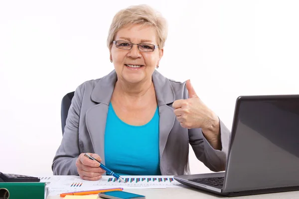 高齢者ビジネスの女性親指を示し事業コンセプトのオフィスで彼女の机で働いて — ストック写真
