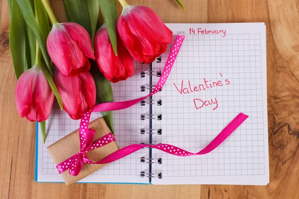 Valentinstag in Notizbuch geschrieben, frische Tulpen und verpacktes Geschenk, Dekoration für Valentinstage — Stockfoto