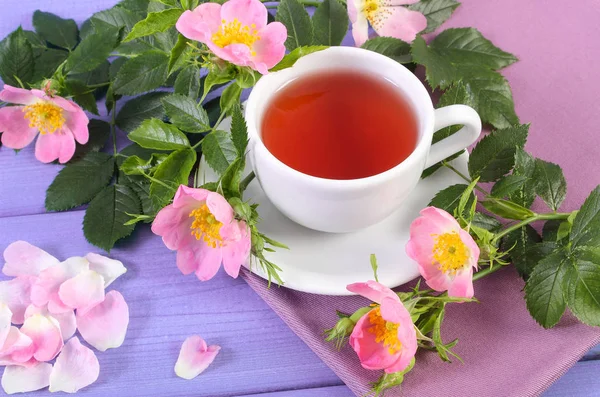 Tasse Tee und Wildrosenblume auf violetten Brettern — Stockfoto