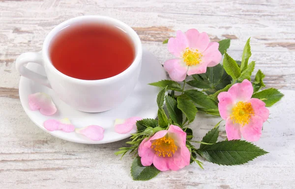 Tasse Tee und Wildrosenblume auf altem rustikalem Holzgrund — Stockfoto