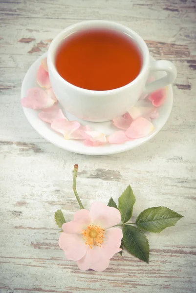 Vintage foto, kopje thee en wild rose bloem op oude rustieke houten achtergrond — Stockfoto