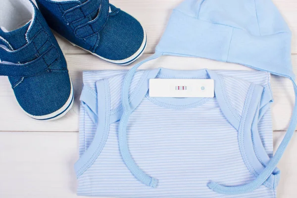 Тест на вагітність з позитивним результатом і одягом для новонароджених, очікуючи на дитину — стокове фото