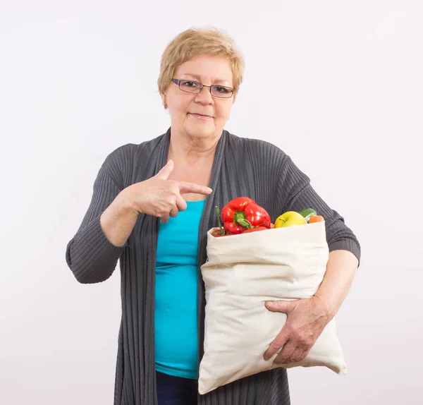 Счастливая пожилая женщина показывает сумку с фруктами и овощами, здоровое питание в старости — стоковое фото