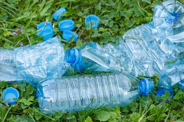 Plastic bottles and bottle caps on grass in park, littering of environment — Stock Photo, Image