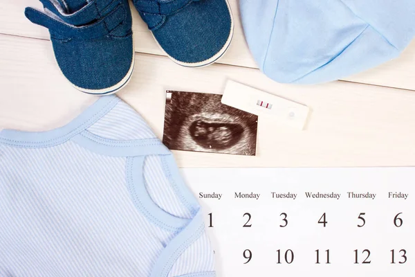 Pregnancy test, ultrasound scan of baby, clothing for newborn and calendar, expecting for baby