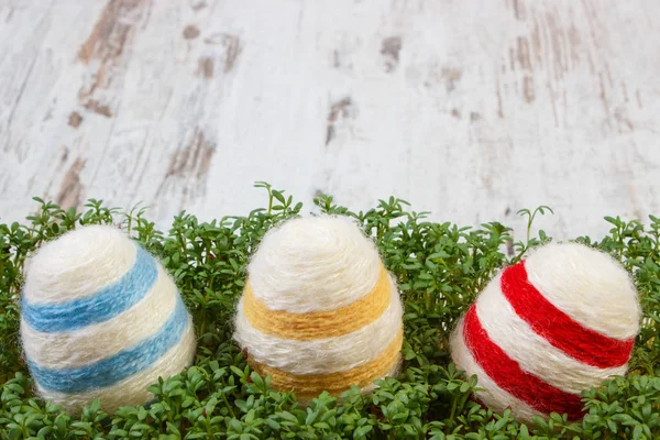 Easter eggs wrapped woolen string and green cress on wooden background, copy space for text, decoration for Easter — Stock Photo, Image