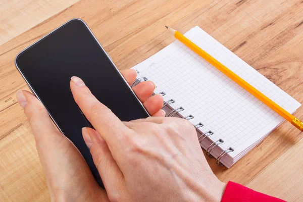 Mão de mulher usando telefone celular, bloco de notas para escrever notas — Fotografia de Stock
