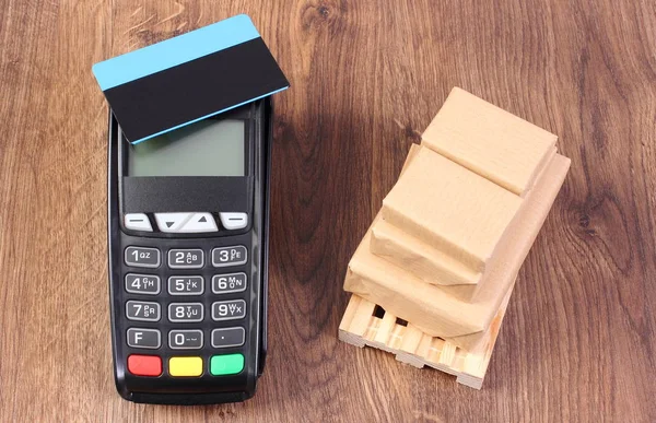 Payment terminal with credit card and wrapped boxes on wooden pallet, paying for products and shipping