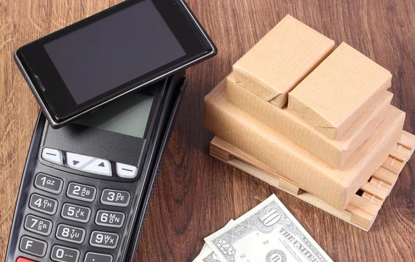 Payment terminal with mobile phone with NFC technology, currencies dollar and wrapped boxes on wooden pallet