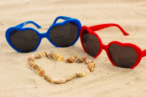 Coração de conchas e óculos de sol na areia na praia — Fotografia de Stock