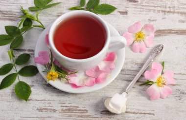 Fincan çay ve eski rustik ahşap arka plan üzerinde yabani gül çiçek